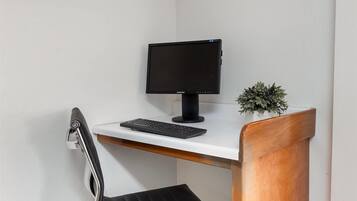 A modern desk with a computer monitor, keyboard, and a small potted plant.