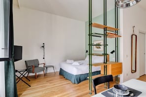 Ett kompakt hotellrum med en säng, ett skrivbord, en stol, en TV och en spegel.