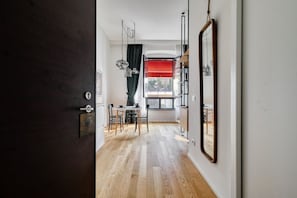 Un pasillo con piso de madera, un comedor con sillas y una mesa, un espejo grande en la pared y una ventana con cortina roja.