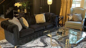 Una sala de estar moderna con un sofá de color oscuro, una mesa de centro de vidrio y una alfombra estampada.