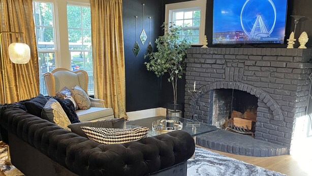 Una sala de estar con un sofá negro, una chimenea y un televisor en la pared.