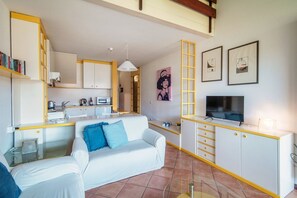 A compact living space with a kitchenette, a sofa, a TV, and artwork on the walls.