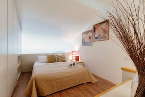 A bedroom with a bed, bedside table, lamp, and artwork.