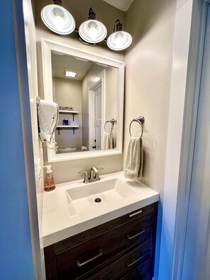A bathroom with a white sink, a mirror, three overhead lights, a towel rack, and a bottle of hand soap. - Blue Ridge Getaway & Spa ~ King | Sauna | Walkable (Black Mountain)