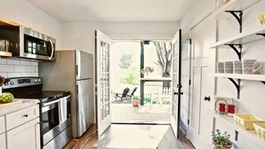 A kitchen with a refrigerator, stove, and microwave. There is a wooden floor and a door leading to an outdoor patio with chairs and plants. - Blue Ridge Getaway & Spa ~ King | Sauna | Walkable (Black Mountain)