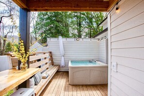 An outdoor patio with a wooden deck, a hot tub, and a wooden bench. - Blue Ridge Getaway & Spa ~ King | Sauna | Walkable (Black Mountain)