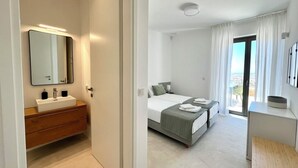 Une chambre d’hôtel moderne avec un grand lit, une table de chevet, une salle de bain avec un lavabo et un miroir, et une vue sur l’extérieur.