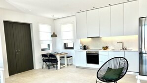Une cuisine moderne avec des meubles blancs, un coin repas comprenant une table et des chaises, et une chaise noire avec un coussin vert.