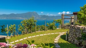 Un jardin avec un mur de pierre, un sentier dallé et une vue sur la mer et les montagnes.