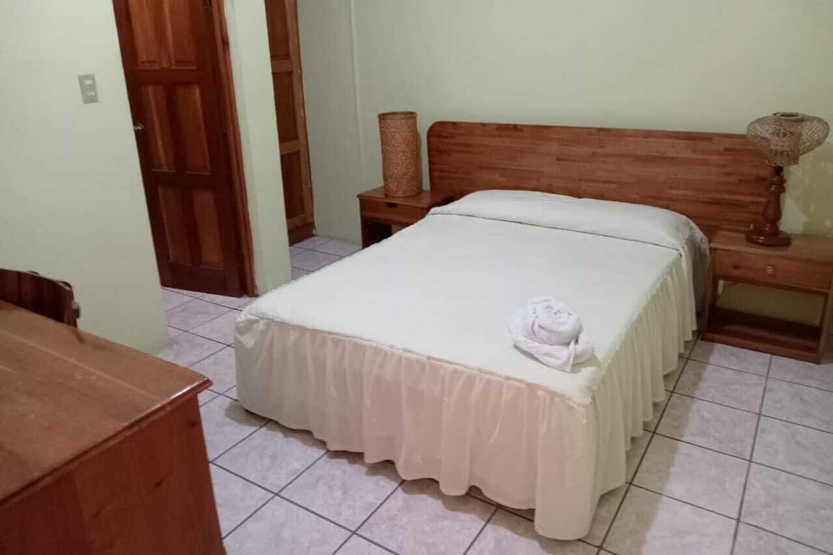 Un dormitorio con cama, mesitas de noche, un armario de madera y una puerta.