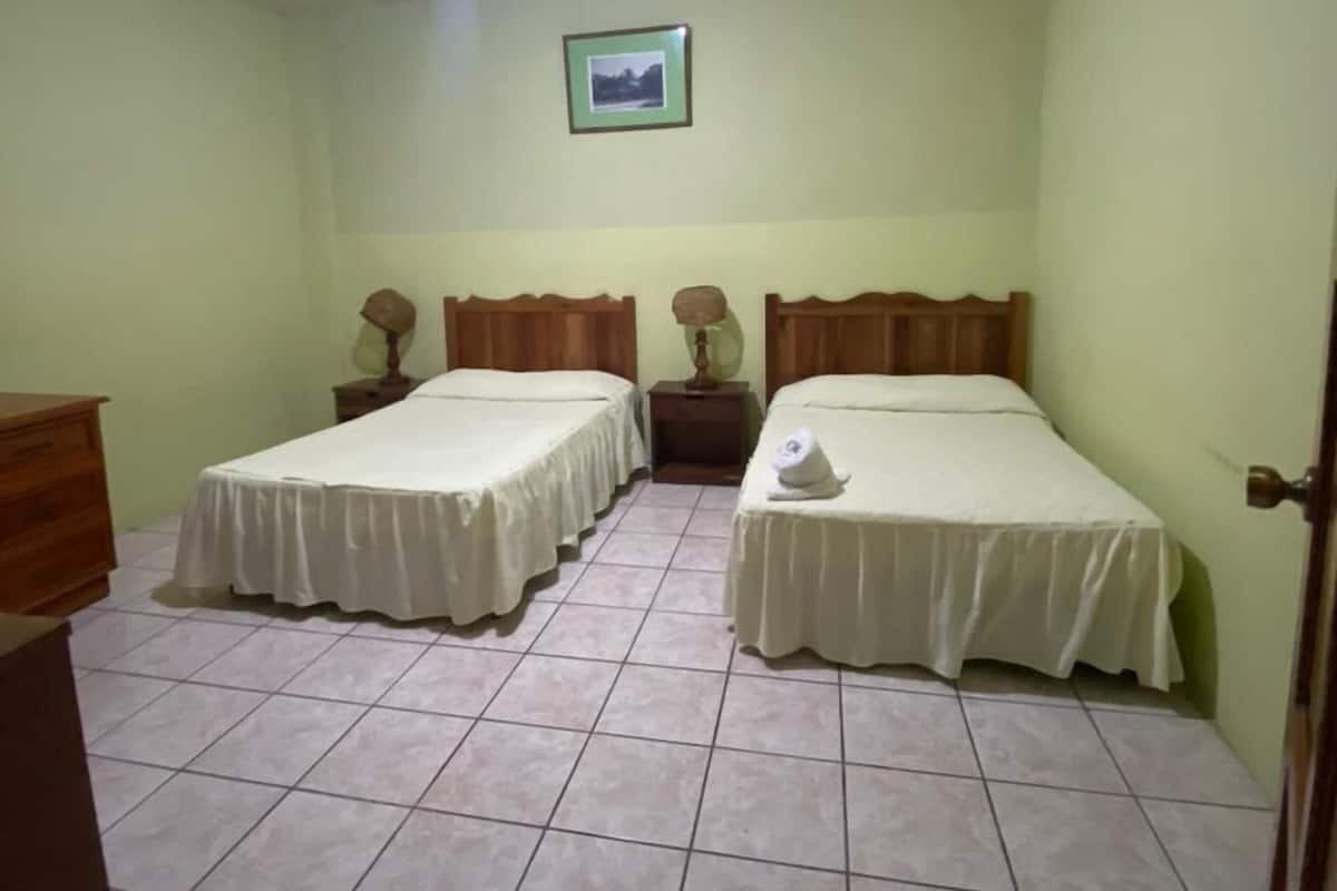 Una habitación con dos camas, un aparador de madera, un cuadro en la pared y una lámpara en el techo.