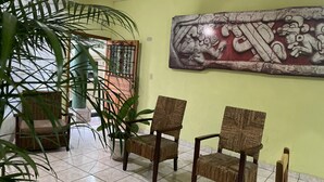 A room with two wicker chairs, a large potted plant, and a wall mural. - Nakum Hotel (Flores)