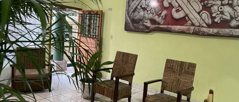 A room with two wicker chairs, a large potted plant, and a wall mural.