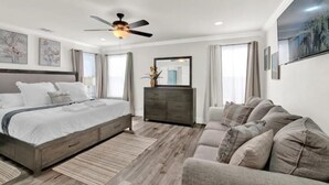 A modern bedroom with a bed, a dresser, a sofa, and a ceiling fan.