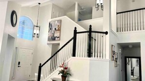 A staircase with white railings and black balusters, a round table with a plant, and a clock on the wall.