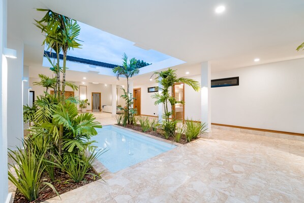 A modern indoor pool area with a skylight, surrounded by tropical plants, and a tiled floor.