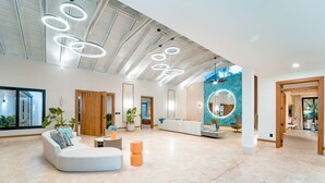 A spacious, modern interior with a large seating area, a circular decorative element on the wall, and a view of the outdoors. - Casa Mangos Casa de Campo DR  (La Romana)
