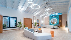 A spacious living area with a modern sofa, a coffee table, and a circular rug. There are potted plants and a large mirror on the wall. - Casa Mangos Casa de Campo DR  (La Romana)