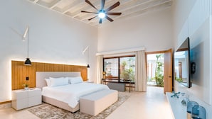 A modern bedroom with a large bed, bedside tables, a desk, and a TV. - Casa Mangos Casa de Campo DR  (La Romana)