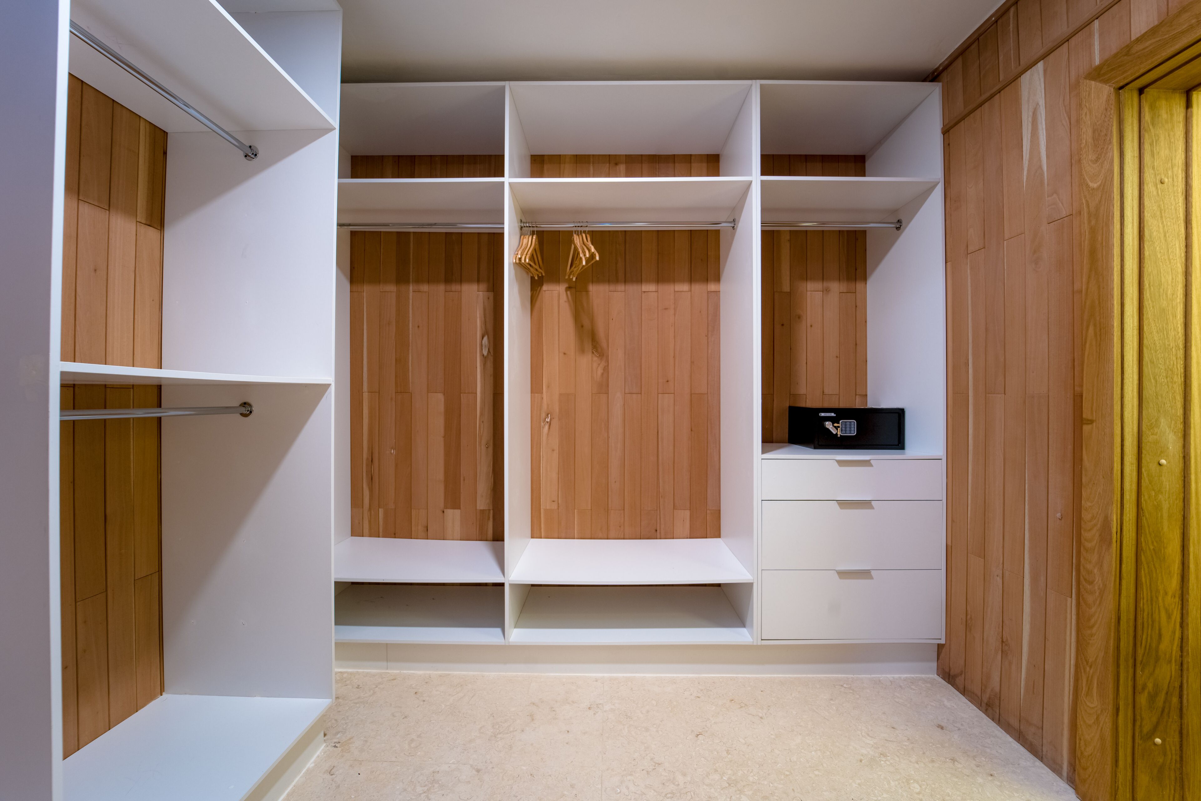 A walk-in closet with wooden paneling, white shelving, and a small desk area.