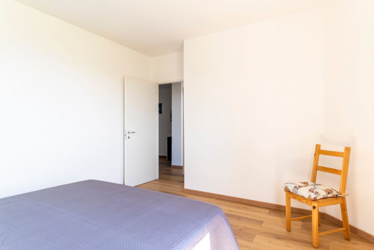 Ein Schlafzimmer mit einem Bett, einem Holzstuhl und einer Tür zu einem anderen Raum.