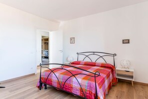 A bedroom with a metal bed frame, a colorful bedspread, a bedside table with a lamp, and a wardrobe.