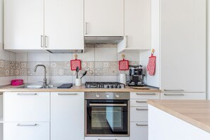 Ett modernt kök med vita skåp, en spis i rostfritt stål och en kakelbeklädd vägg bakom arbetsbänken.