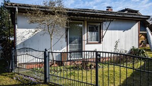 Ein Haus mit weißer Fassade, einem schwarzen Metallzaun und einem kleinen Garten mit violetten Blumen.