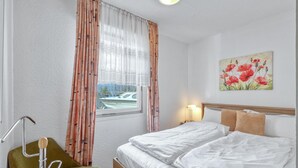 Ein Hotelzimmer mit Bett, Stuhl, einem Bild und einem Fenster mit Blick auf ein Boot.