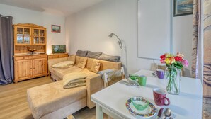 Ein gemütliches Wohnzimmer mit einer Couch, einem Esstisch mit Blumenvase und einem Holzschrank.