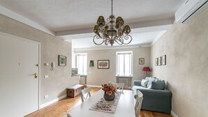 A dining area with a white table, chairs, a chandelier, and a sofa in the background. - GuestHost - Modern Apartment in the heart of Lucca! (Lucca)