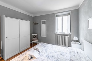 Una camera da letto con un letto, un armadio, un termosifone, una finestra e una sedia.