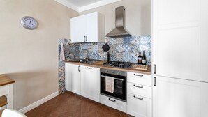 A kitchen with white cabinets, a stove, oven, and a clock on the wall. - GuestHost - Modern Apartment in the heart of Lucca! (Lucca)