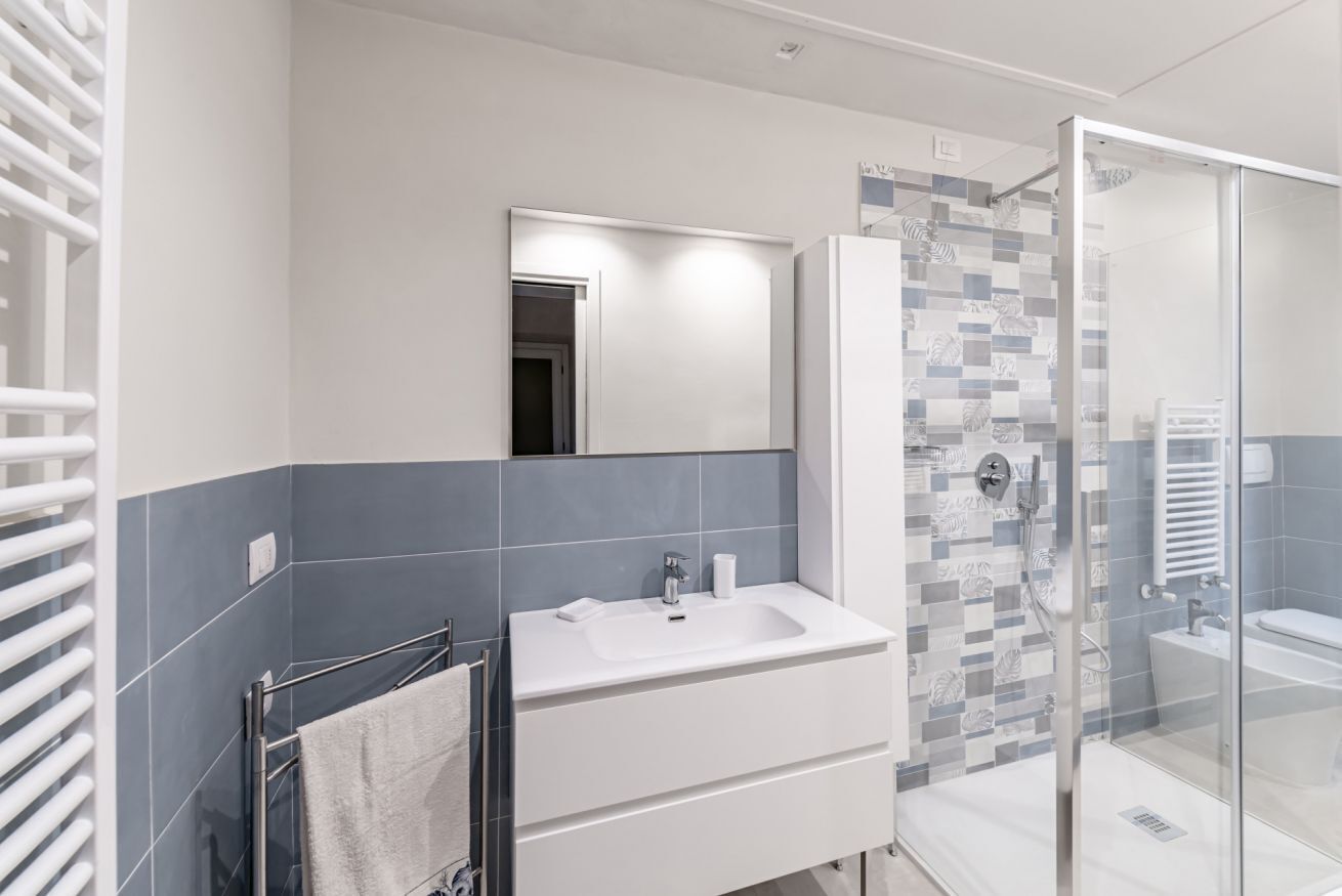 A modern bathroom with a white sink, a glass shower enclosure, and a towel rack.