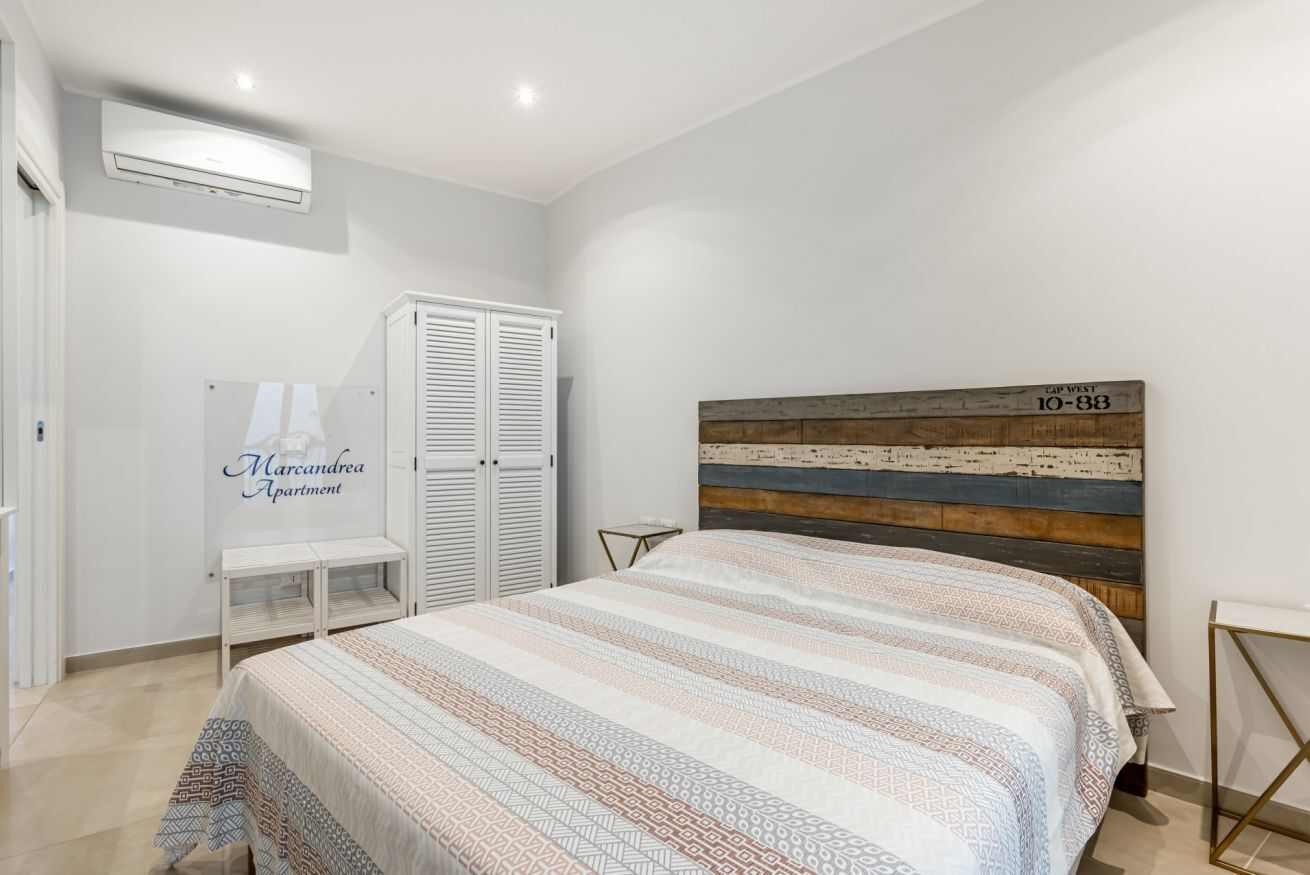 A bedroom with a bed, a wardrobe, a bedside table, and a wall-mounted air conditioner.
