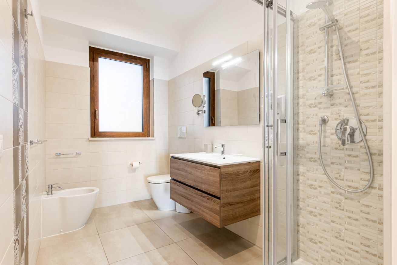 Een moderne badkamer met een douchecabine van glas, een vrijstaand bad, een toilet en een wastafel met spiegel.