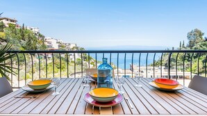 Ein Holztisch mit Tellern und Gläsern, eine blaue Flasche und Blick auf Meer und Häuser.