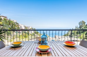 A wooden table with plates and glasses, a blue bottle, and a view of the sea and buildings.