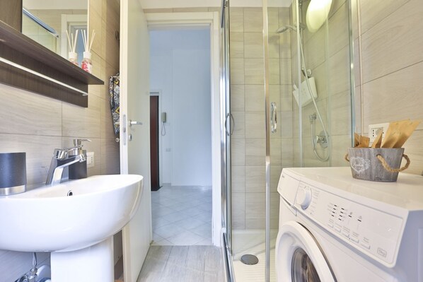 Un baño con lavamanos, espejo, ducha y lavadora.