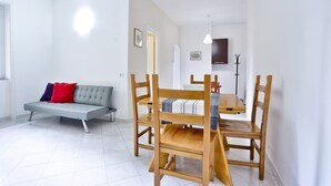 A modern living room with a sofa, dining table, chairs, and a coat rack.