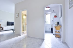 A modern living room with a flat-screen TV, a dining area, and a kitchen with a white fridge and shelves. - Bella Ma' Enjoyable Apartment (Salerno)