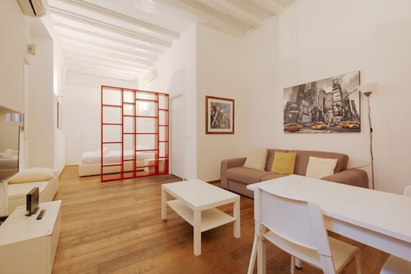 Una sala moderna con un sofá, una mesa de comedor y una mesa de centro. Hay un separador rojo y un cuadro en la pared.