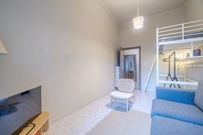 Un soggiorno moderno con televisione, una sedia bianca, un divano blu e un letto a castello.