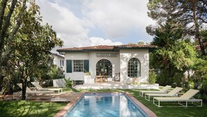 Una casa con piscina, rodeada de césped cuidado y árboles.