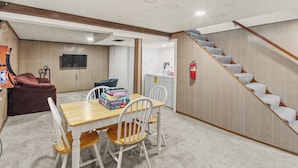 Una habitación acogedora con una escalera de madera, un comedor con mesa y sillas, un televisor y un extintor en la pared.