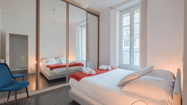 Et moderne hotelværelse med en stor seng, en blå stol, et spejl og udsigt over byen fra vinduet.