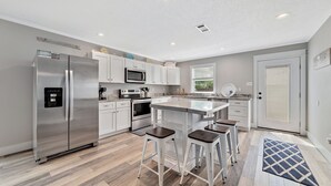 Una cocina moderna con un refrigerador de acero inoxidable, armarios blancos, un microondas y una isla grande con taburetes de bar.