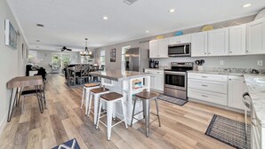 Una cocina moderna con gabinetes blancos, electrodomésticos de acero inoxidable y una isla central con taburetes de bar.