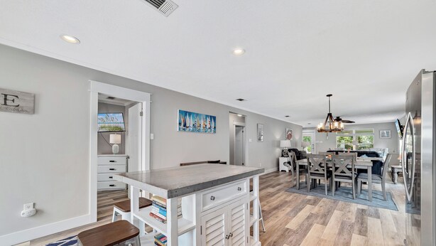 Una cocina moderna con una isla central, armarios blancos y una zona de comedor con mesa y sillas.