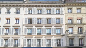 A multi-story building with a row of windows, some with shutters, and a blue awning with the text "ANTIQUEITES ETIENNE LEVY". - Sublime Loft à St Germain (6pax) (Paris)